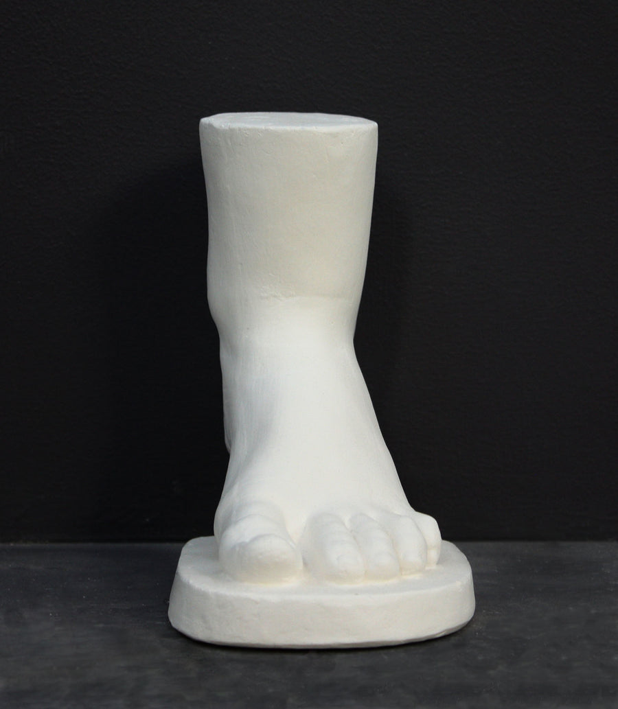 photo of white plaster cast sculpture of child foot against gray background