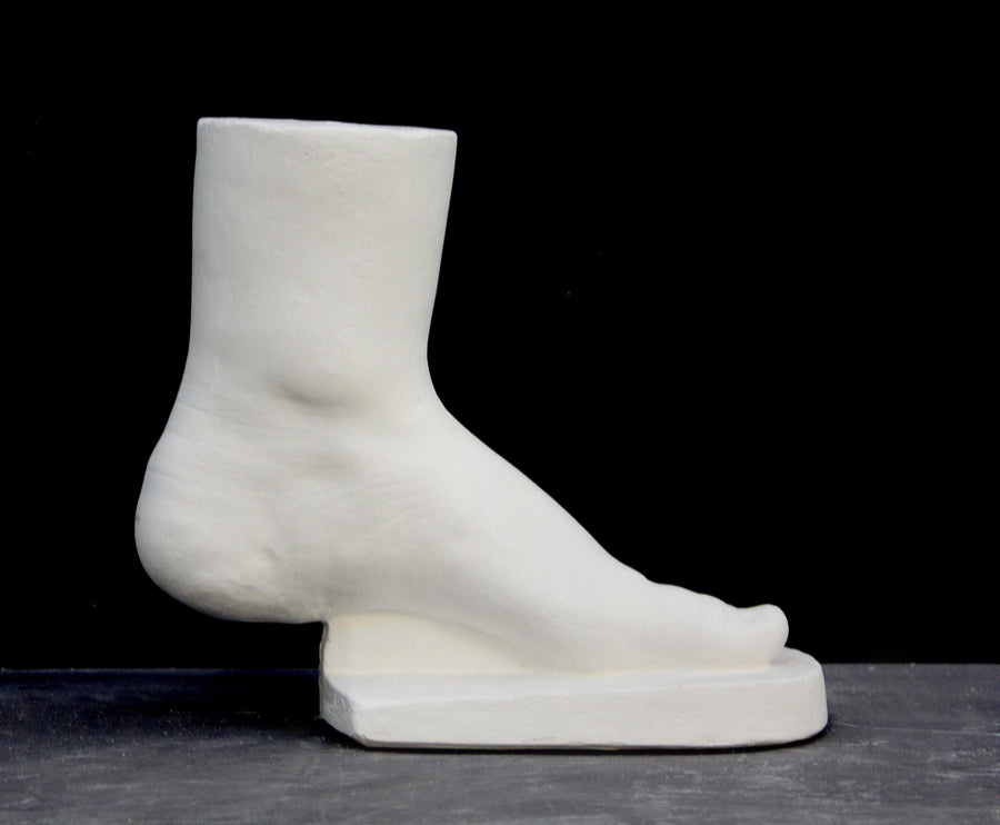 photo of white plaster cast sculpture of child foot against gray background