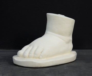 photo of white plaster cast sculpture of baby foot against gray background
