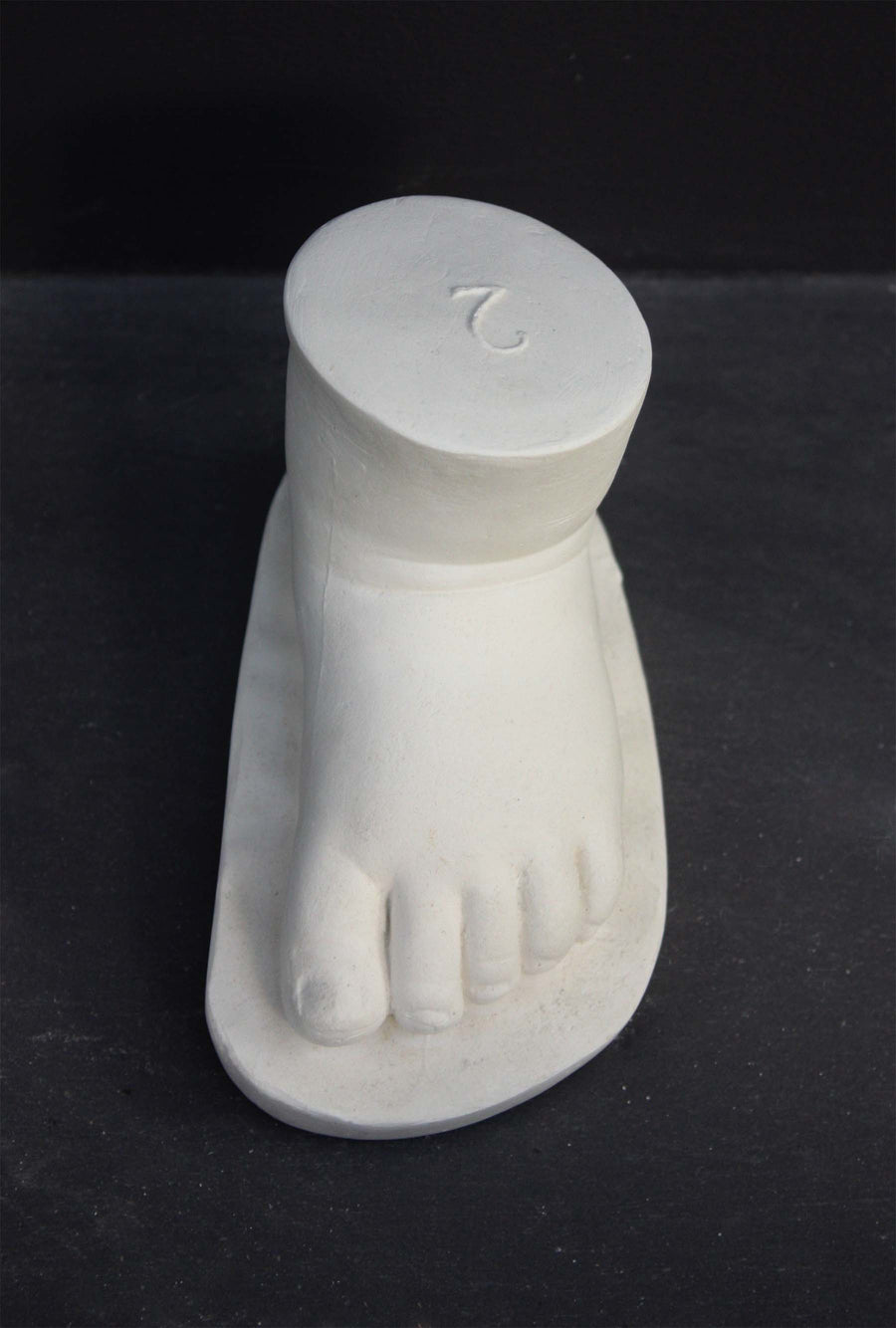 photo of white plaster cast sculpture of baby foot against gray background