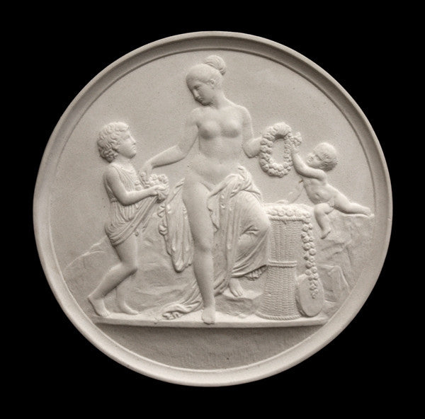 photo of off-white plaster cast relief sculpture of mostly nude female figure with two children and flowers and wreaths against black background