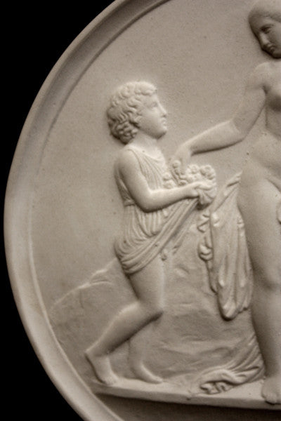 closeup photo with black background of plaster cast relief sculpture of child giving flowers to a mostly nude female figure