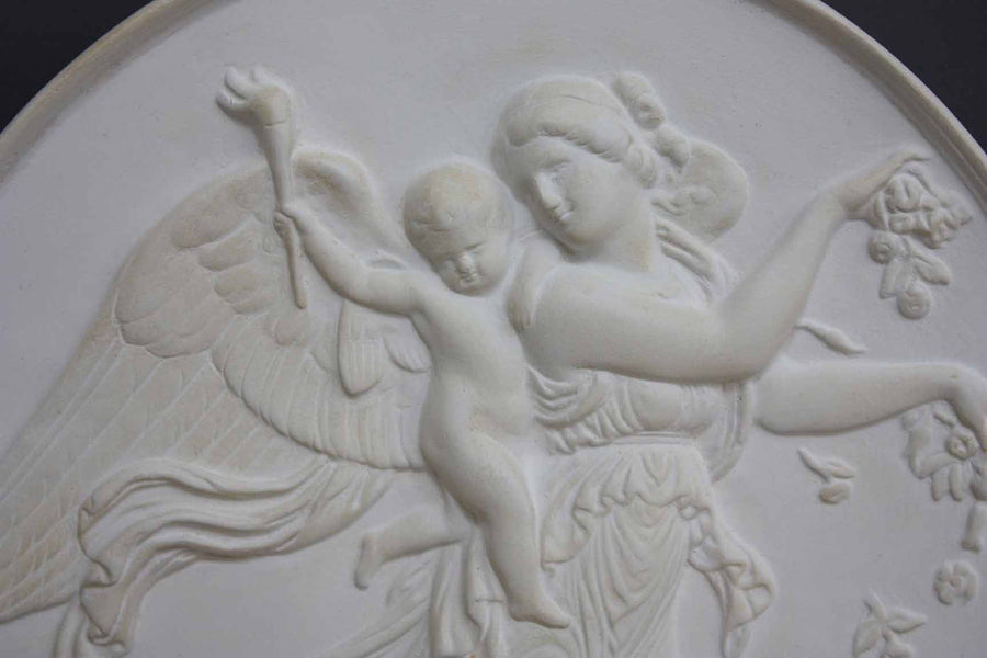 photo with gray background of plaster cast relief of female with wings flying and a cherub on her back