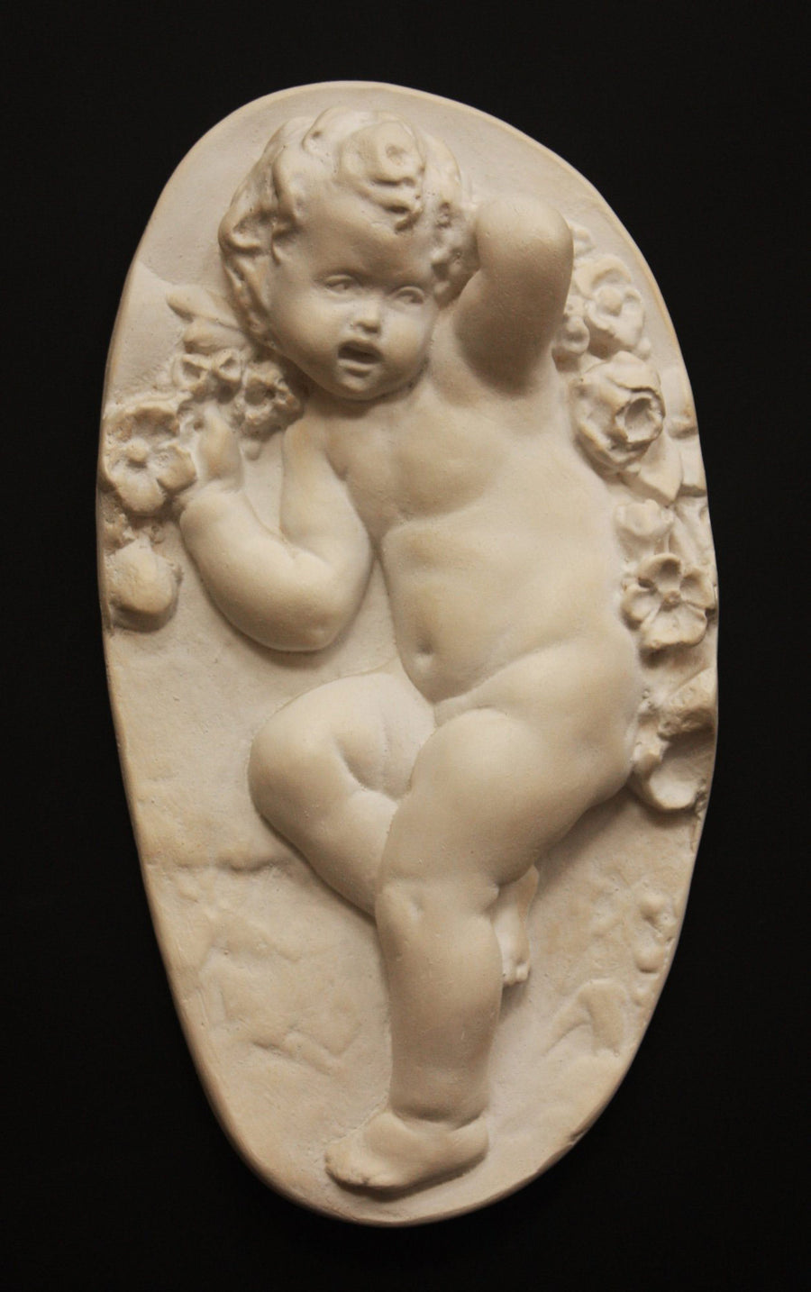 photo with black background of plaster cast relief of child dancing with a garland