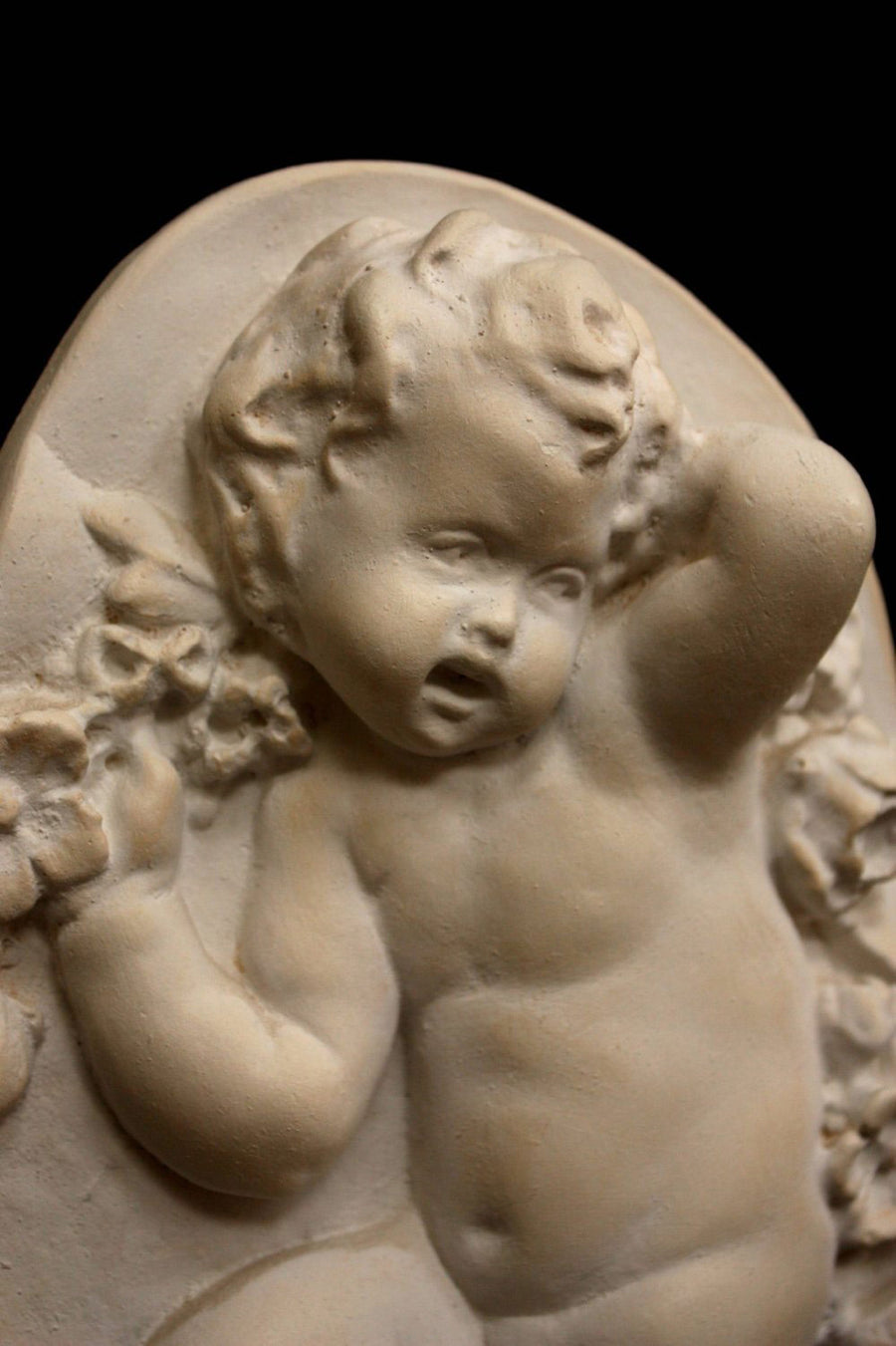 photo with black background of plaster cast relief of child dancing with a garland