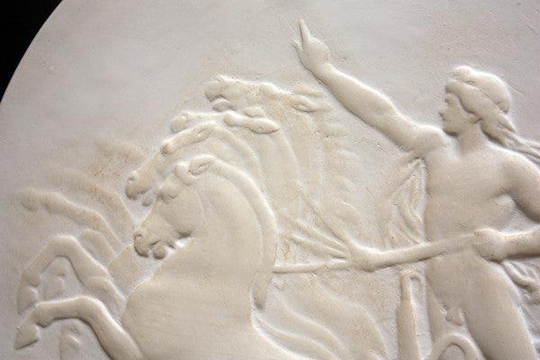 closeup photo of plaster cast relief sculpture of nude male figure in horse-drawn chariot flying