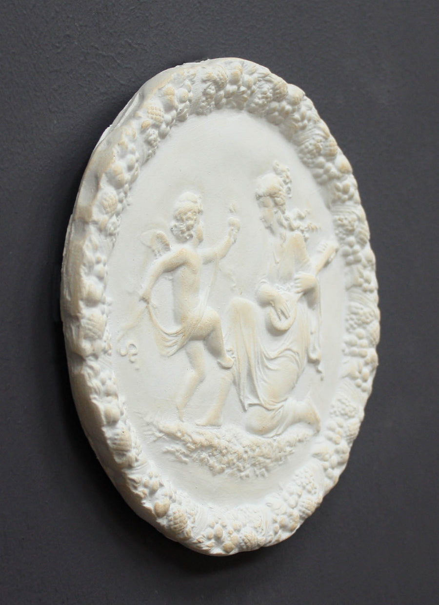 photo of white plaster cast relief sculpture of a child dancing and a female figure playing an instrument against dark gray background