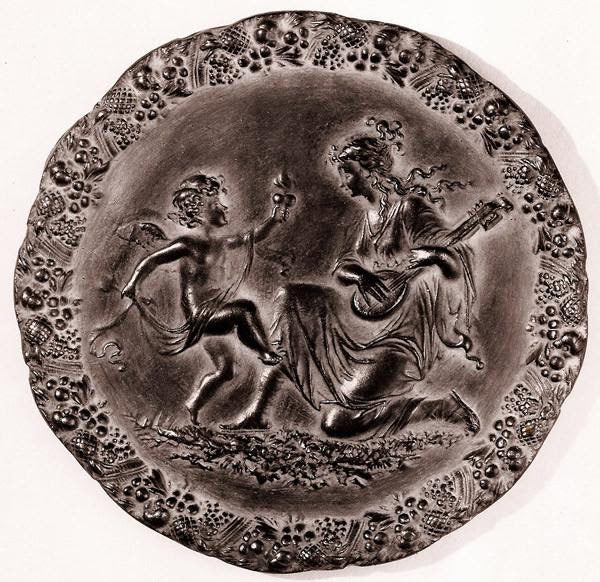photo with tan background of bronze-colored plaster cast relief sculpture of a child dancing and a female figure playing an instrument