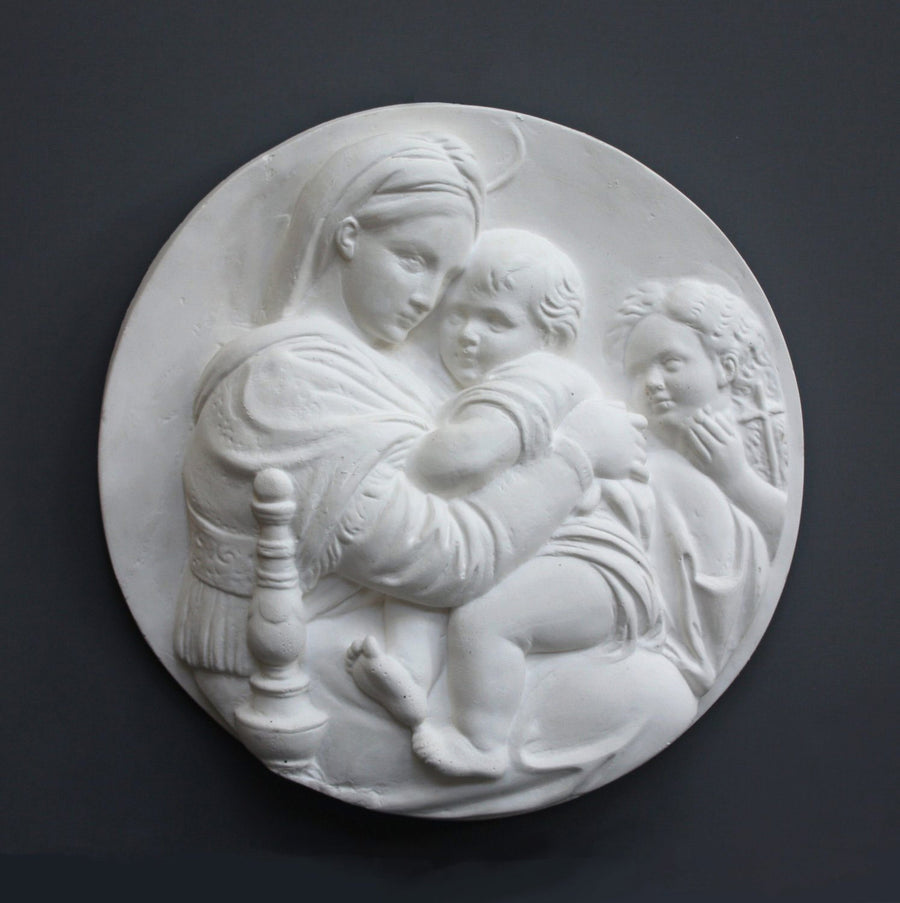 photo of relief plaster cast featuring the Madonna, Child, and St. John and hanging on a dark-colored wall