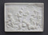 photo of plaster cast relief of one satyr and eight children wrestling and playing instruments with trees and domed building in the background on a gray background