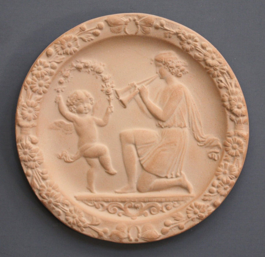 photo with gray background of plaster cast of small relief with a dancing child and a young man playing two horns