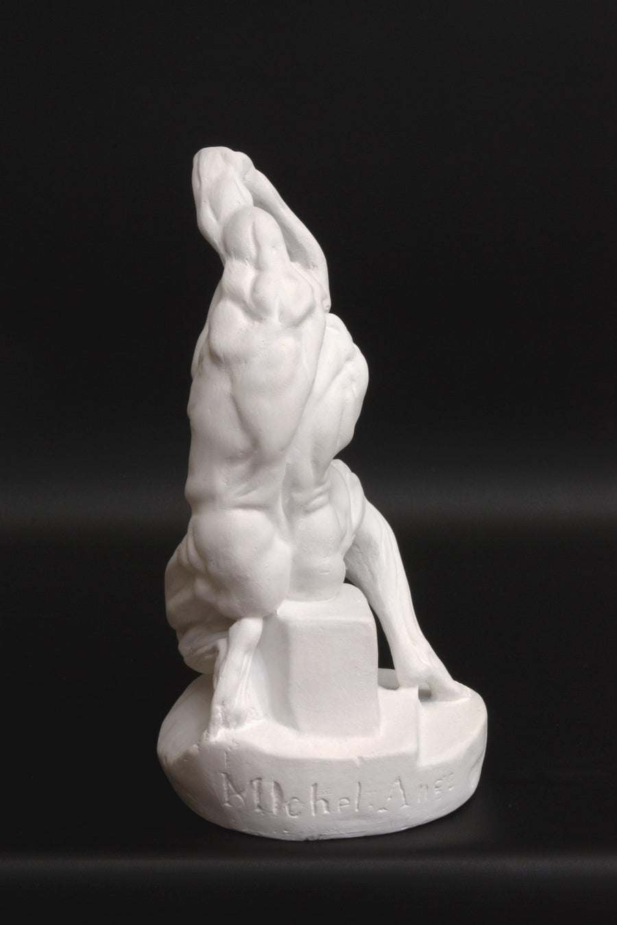 Photo of plaster cast sculpture of flayed man kneeling with hands on head on black background