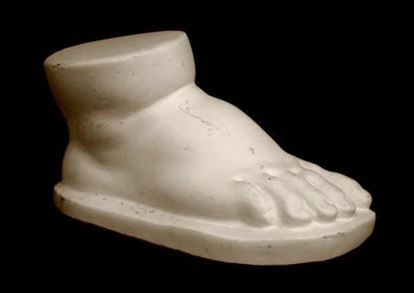 photo of off-white plaster cast sculpture of baby foot against black background