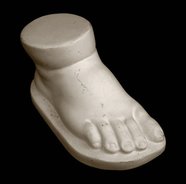 photo of off-white plaster cast sculpture of baby foot against black background