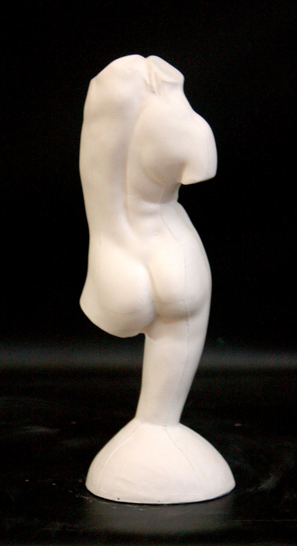 photo of plaster cast sculpture of female torso and right leg flowing into plaster base against black background