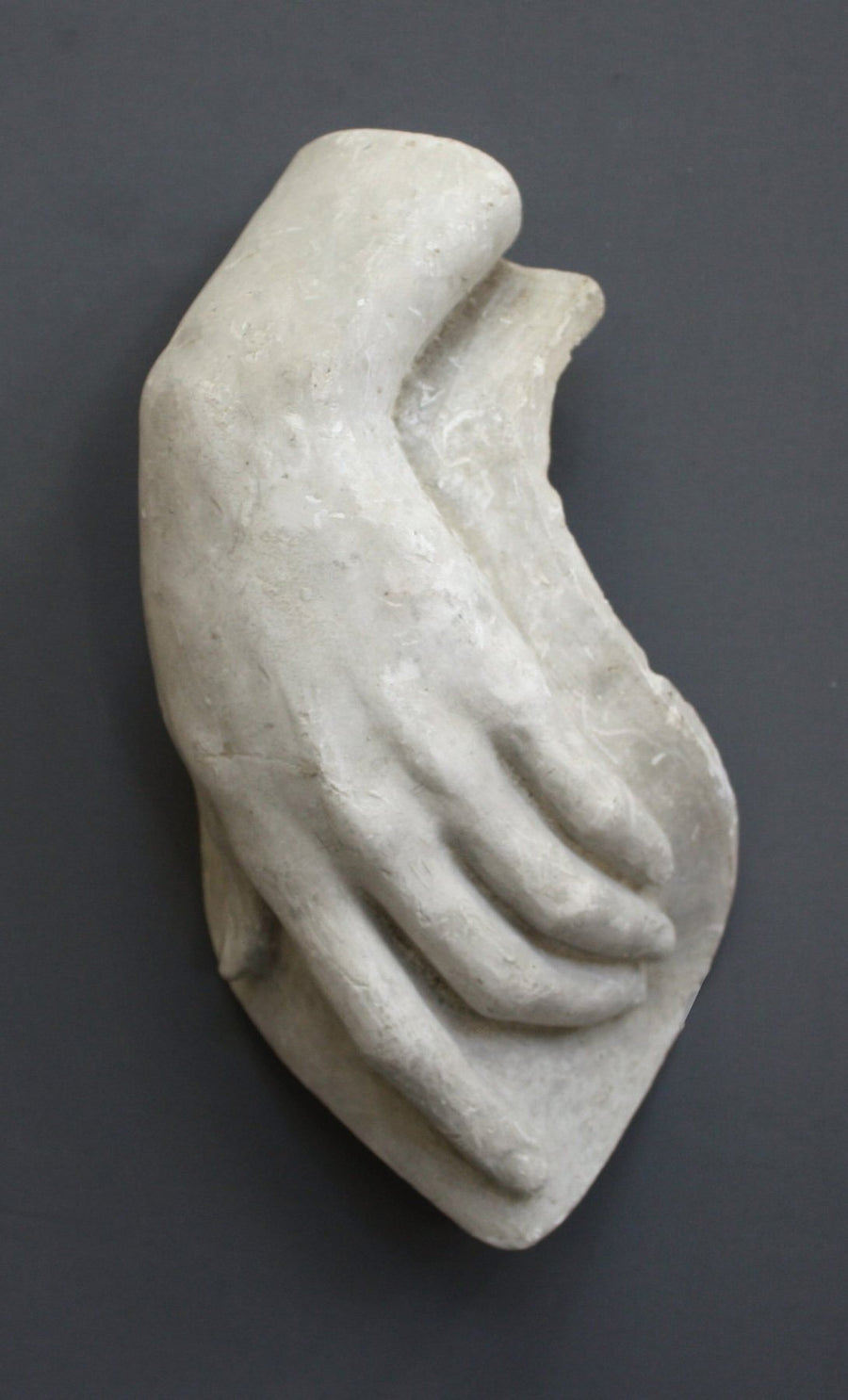 photo with gray background of plaster cast sculpture of female left hand on a curved panel with fingers curled except index finger that points