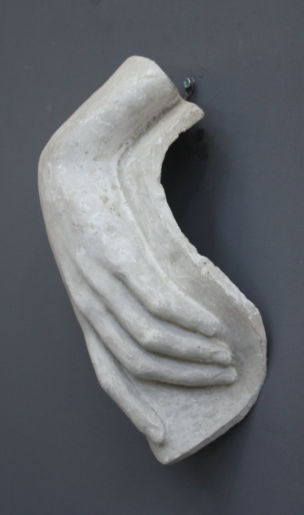 photo with gray background of plaster cast sculpture of female left hand on a curved panel with fingers curled except index finger that points