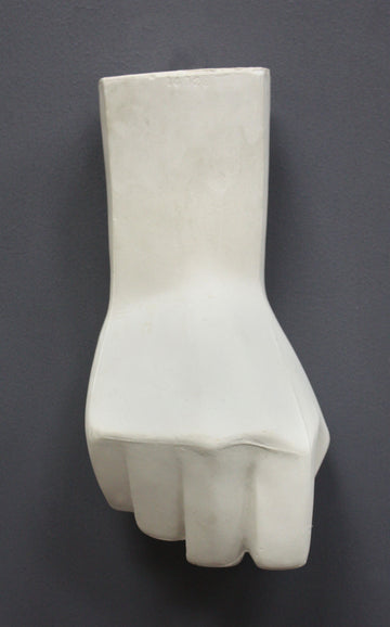 photo of white plaster cast sculpture of hand in fist in block forms against gray background