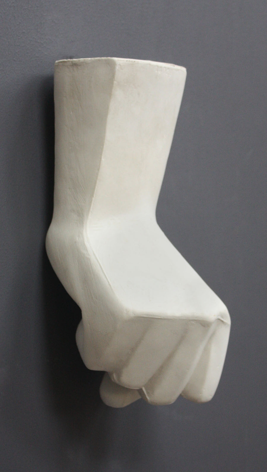 photo of white plaster cast sculpture of hand in fist in block forms against gray background