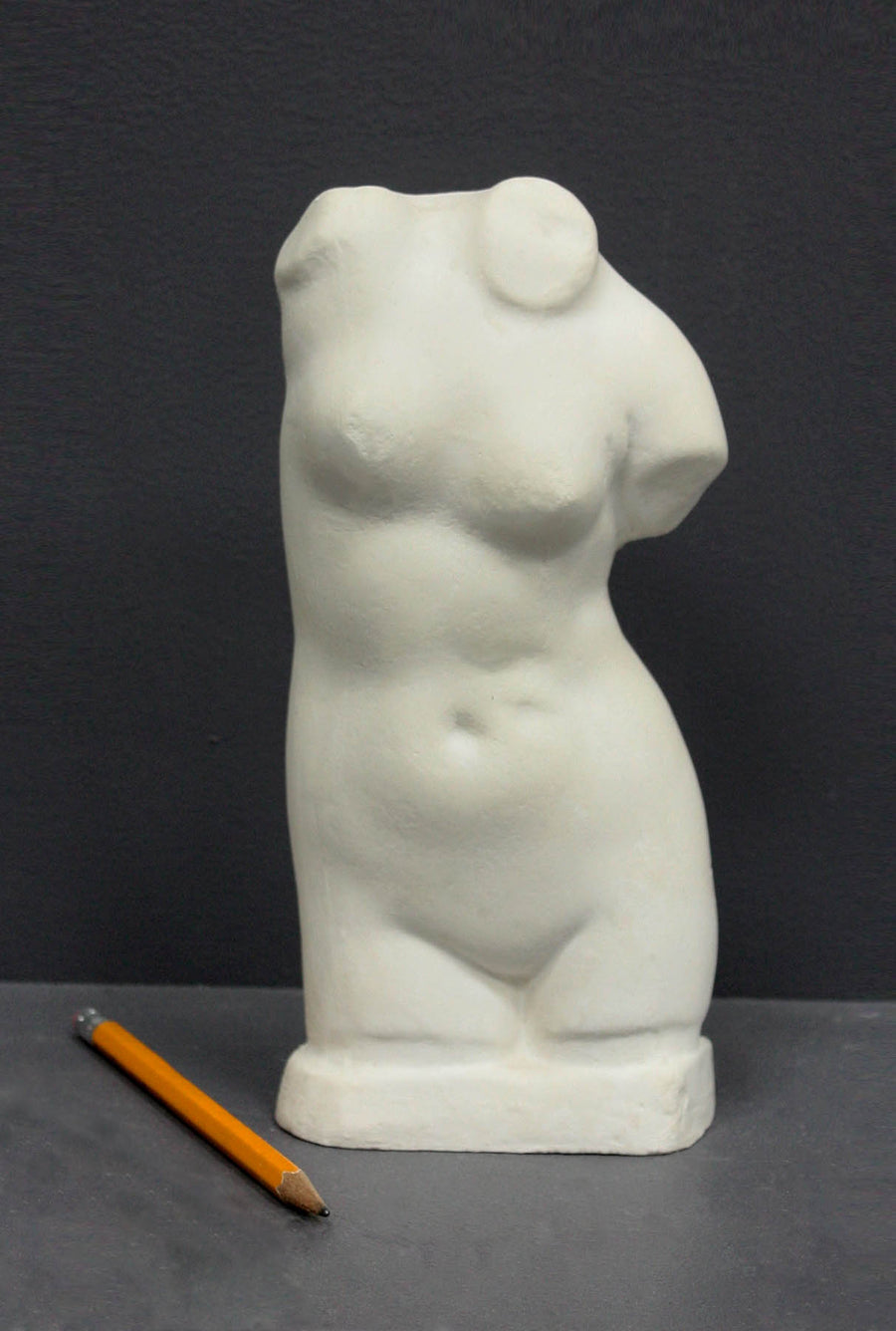 photo of off-white plaster cast sculpture of female torso and yellow pencil beside it against dark gray background