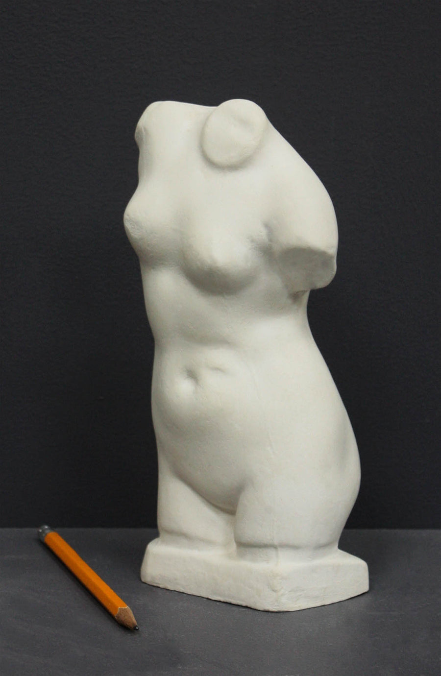 photo of off-white plaster cast sculpture of female torso and yellow pencil beside it against dark gray background