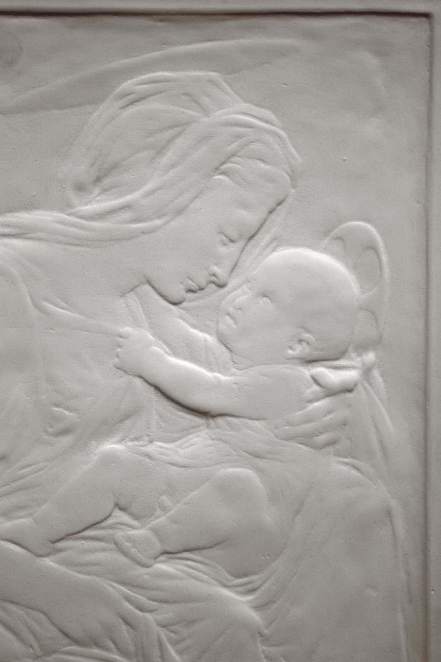 photo detail of plaster cast sculpture relief of the Madonna holding baby Jesus on her lap on black background