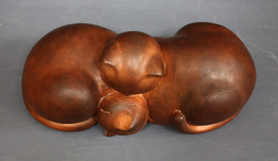 Top view photo with gray background of brown plaster cast sculpture of two cats sleeping with their heads nestled together