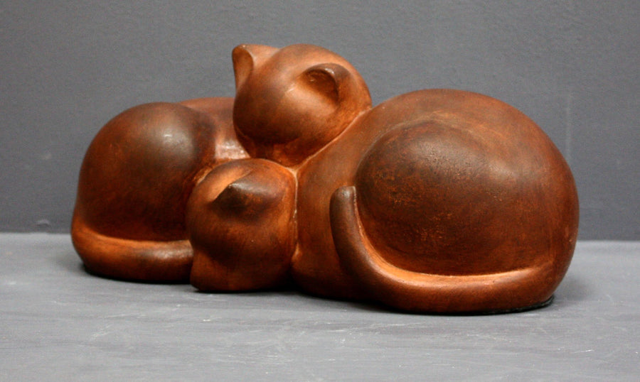 Photo with gray background of brown plaster cast sculpture of two cats sleeping with their heads nestled together from a slight angle