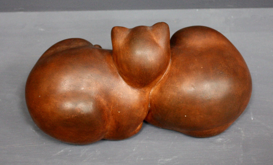 Photo with gray background of brown plaster cast sculpture of two cats sleeping with their heads nestled together