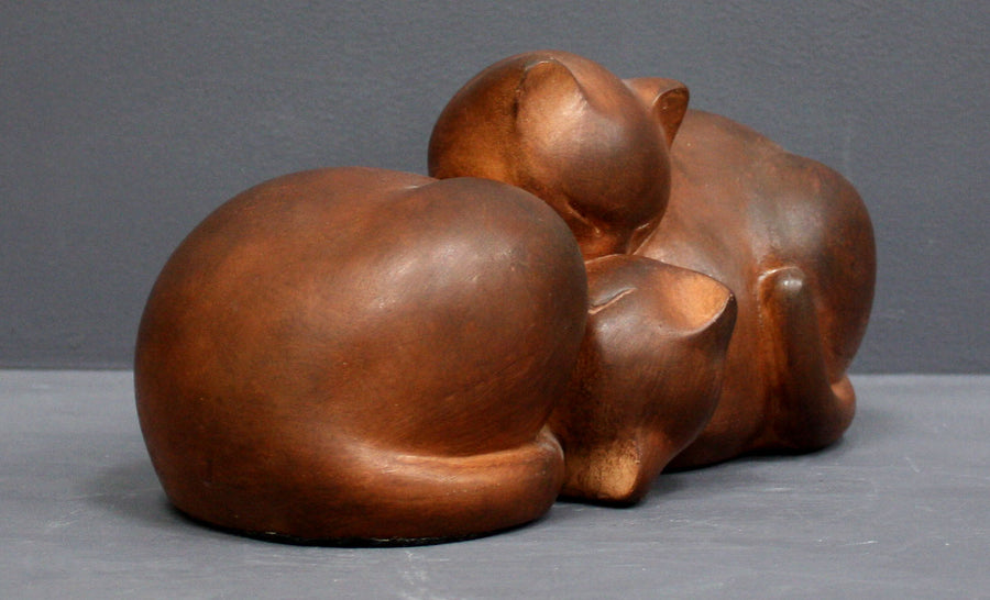 Photo with gray background of brown plaster cast sculpture of two cats sleeping with their heads nestled together