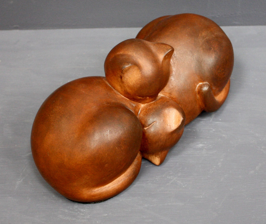Photo with gray background of brown plaster cast sculpture of two cats sleeping with their heads nestled together