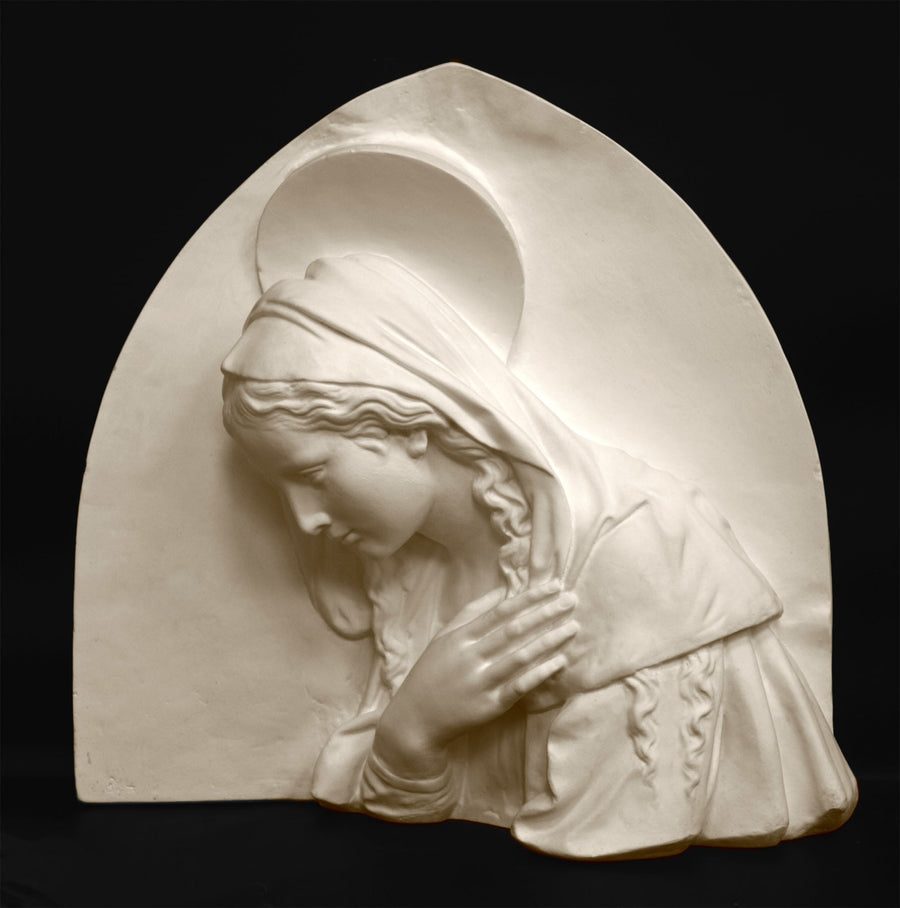 photo of plaster cast sculpture relief of the Madonna leaning over with her right hand crossed over her chest and a halo above her head on a black background