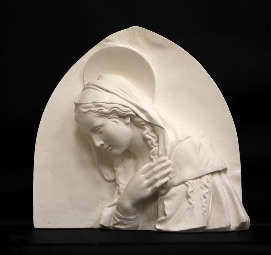 photo of plaster cast sculpture relief of the Madonna leaning over with her right hand crossed over her chest and a halo above her head on a black background