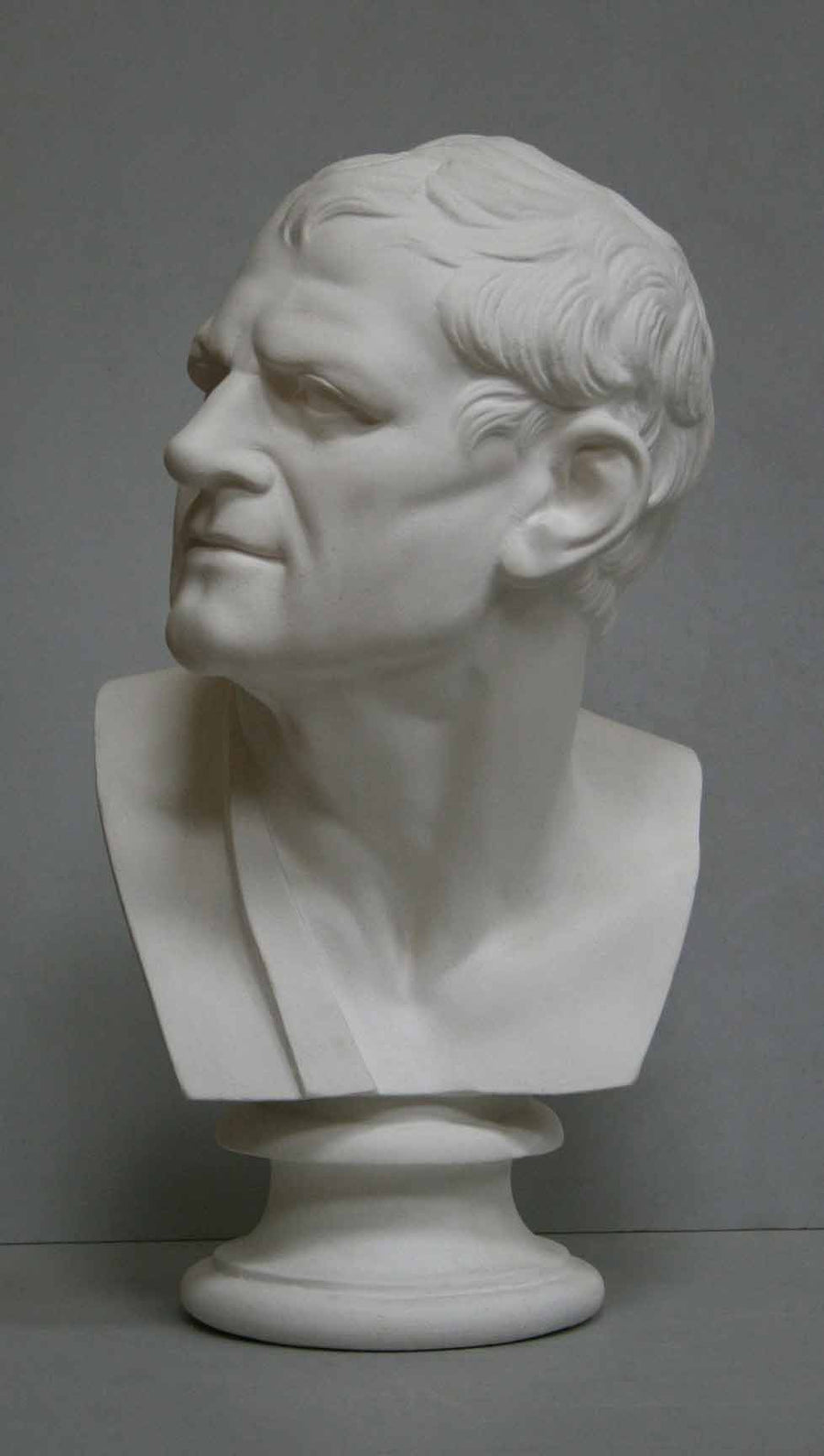 photo of plaster cast bust of man with head turned to his right and a sash on his right shoulder on a gray background