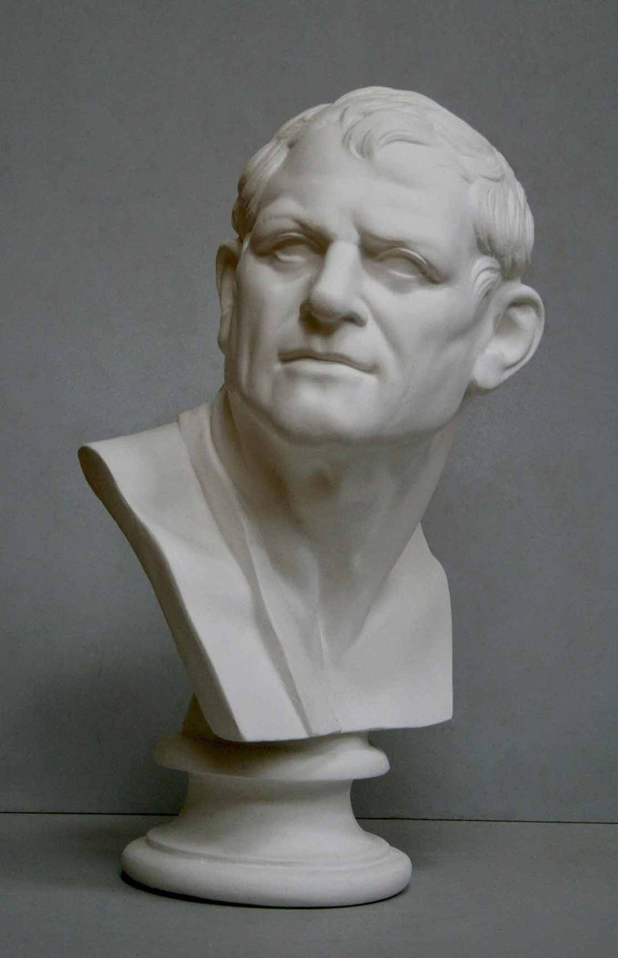 photo of plaster cast bust of man with head turned to his right and a sash on his right shoulder on a gray background