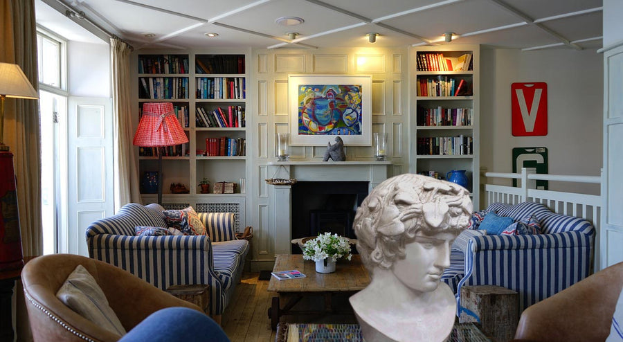 Photo of a colorful living room with blue striped sofas, fireplace, and bookshelves and a plaster cast sculpture of male head of Antinous with crown of leaves in the foreground