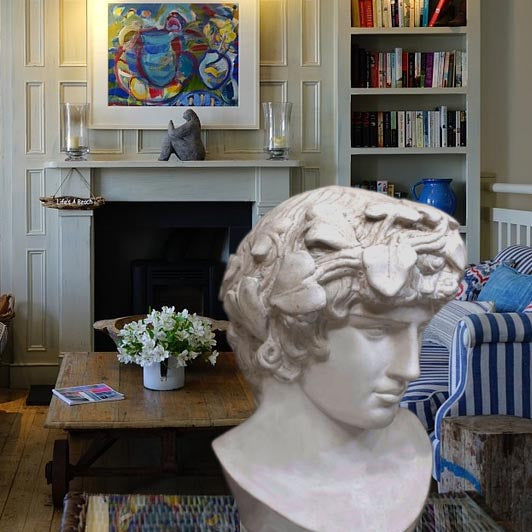 Photo of a colorful living room with blue striped sofas, fireplace, and bookshelves and a plaster cast sculpture of male head of Antinous with crown of leaves in the foreground