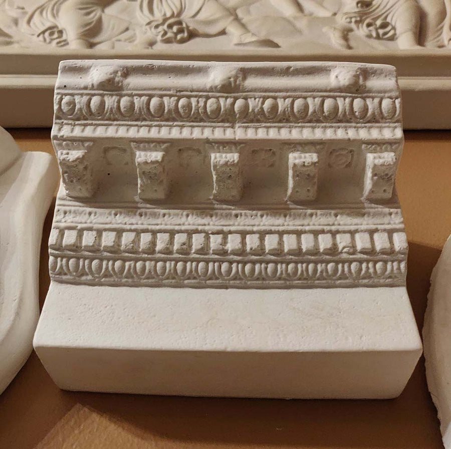 Photo of plaster cast of ornamental architectural detail on gold wall with nearby plaster casts