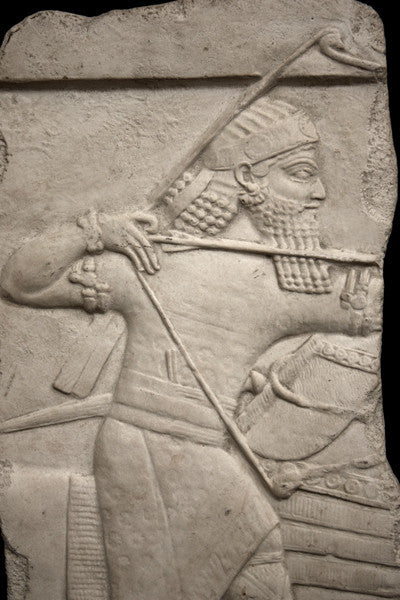 photo of plaster cast relief sculpture of King Ashurbanipal on horseback (only midsection of horse visible) and aiming an arrow in front of him on a black background