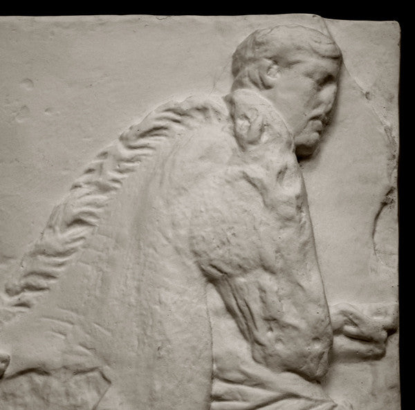 closeup photo of off-white plaster cast relief sculpture of three men on horseback from Parthenon against black background