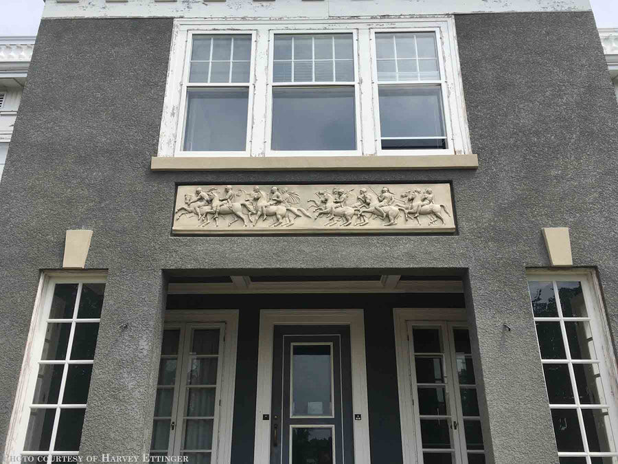 photo of plaster cast relief sculptures of men on horses above doorway on facade of gray house