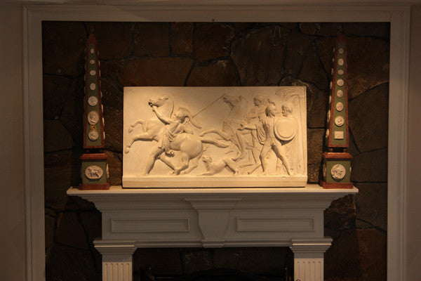 photo of plaster cast relief of men, some with armor, horses, and a dog over a fireplace with a stone wall
