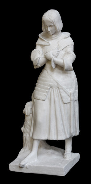 photo with black background of plaster cast sculpture of Joan of Arc standing in armor with arms crossed at her chest