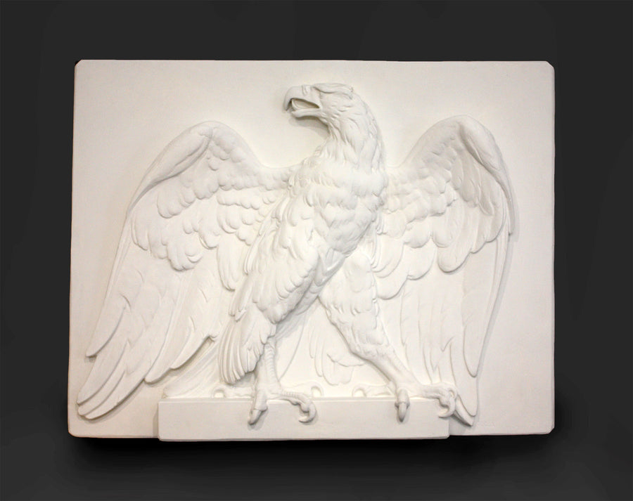 photo of white plaster cast of relief sculpture of an eagle calling, with its head turned toward the right and its wings open on gray background