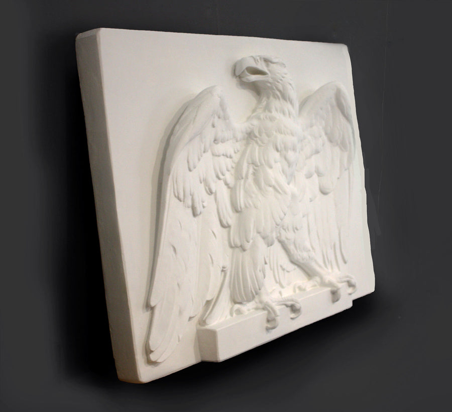side photo of white plaster cast of relief sculpture of an eagle calling, with its head turned toward the right and its wings open on gray background