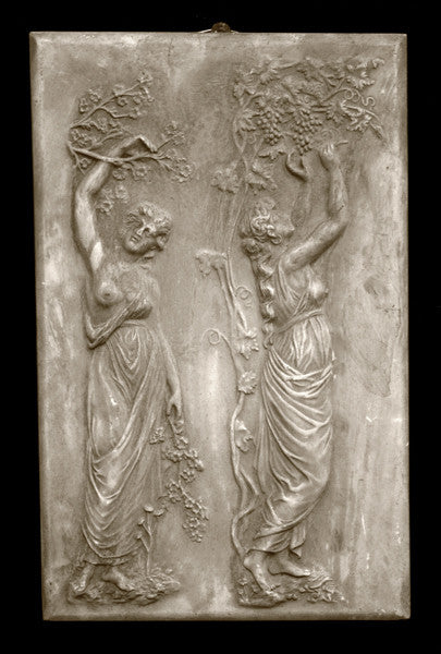 photo with black background of yellowed plaster cast relief sculpture of two robed female figures touching tree branches above their heads