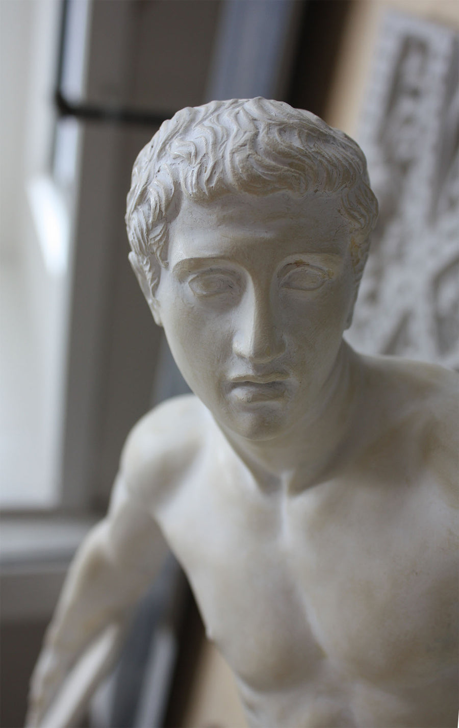 Photo closeup of face of plaster cast of nude male athlete readying to throw a discus