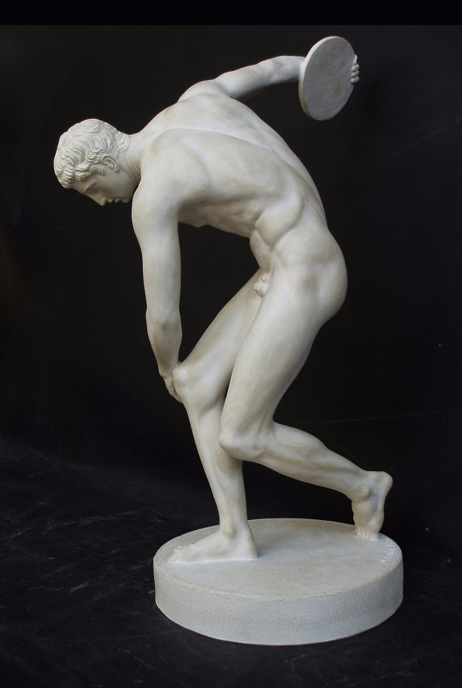 Photo with black background of plaster cast of nude male athlete readying to throw a discus