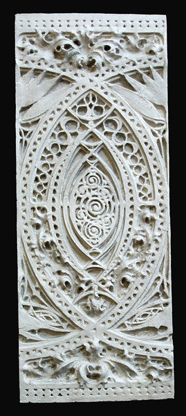 photo of white plaster cast of architectural ornament with geometric lines and leaf patterns against black background