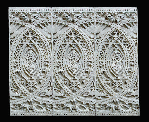photo of white plaster cast of architectural ornament with geometric lines and leaf patterns in a row against black background